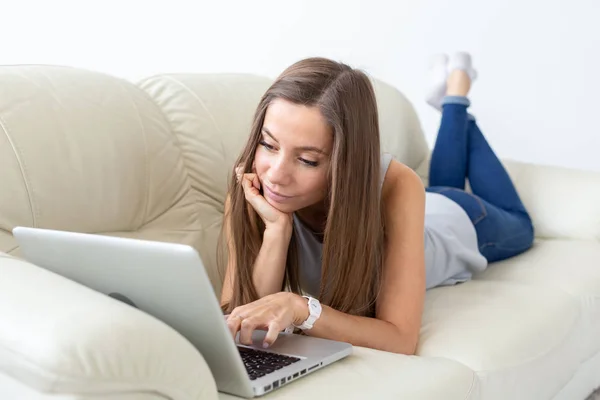 Technologie, zrelaksować się i zewnętrznych, koncepcja - młoda kobieta, leżąc na kanapie i pracę na laptopie — Zdjęcie stockowe