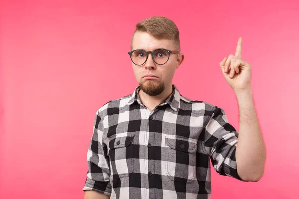 Attraktiver, lustiger junger Mann mit Brille und kariertem Hemd, der mit dem Finger auf rosa Hintergrund zeigt — Stockfoto
