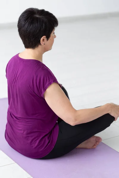 Yoga, harmony, people concept - Middle aged woman sitting in lotus position, close up back view