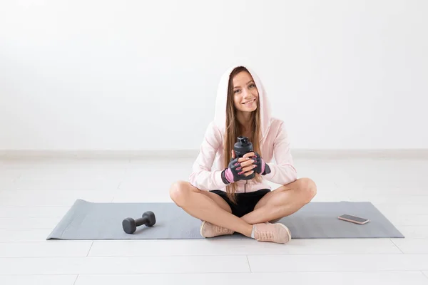 Estilo de vida saludable, personas y concepto deportivo - Mujer sentada en una esterilla de yoga y bebiendo agua después de un duro entrenamiento — Foto de Stock