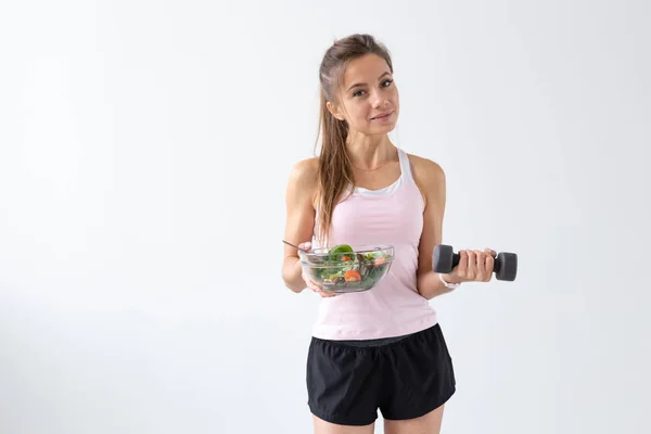 Egészséges életmód, az emberek koncepció - egy tányér saláta az egyik kezében, és a súlyzó, a másik kezében. Mosoly és fitness ruha — Stock Fotó