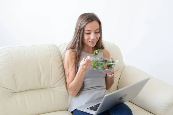Healthy lifestyle, proper diet, relax and people concept- young beautiful woman sitting on the white sofa and eating a salad