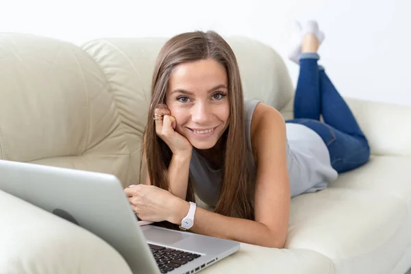Koncepcja technologii, freelance i ludzie - młoda kobieta, leżąc na kanapie z laptopem i patrząc na kamery — Zdjęcie stockowe