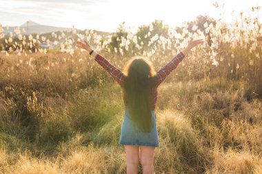 Yaz, özgürlük ve tatil kavramı - doğa ve güneş ışığı ve saman alan, yükseltilmiş kollarında genç kadının arkadan görünüm