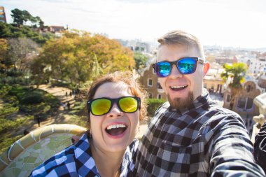 Komik genç çift kamera ile akıllı telefon Park Guell, Barselona, İspanya, gülümseyen fotoğrafı çekmek.