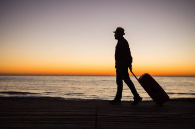 Tatil, yaz ve seyahat kavramı - genç adam siluet çanta batımında denize yakın