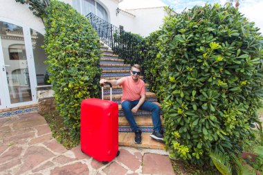 Tatil, seyahat ve Bagaj konsepti - çanta merdivenlerde oturan genç adam