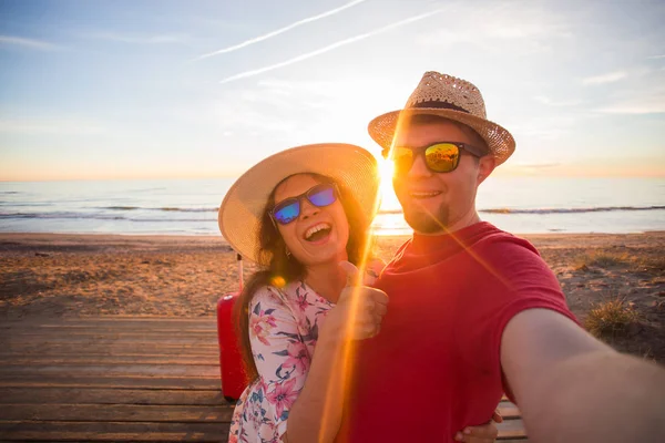 Glückliches reisendes verliebtes Paar, das an einem sonnigen Sommertag ein Handy-Selfie mit Koffern am Strand macht — Stockfoto