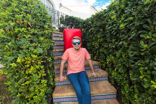 休日、旅行および人々 のコンセプト - 彼の家の階段に座っている赤い旅行かばんを持つ男 — ストック写真