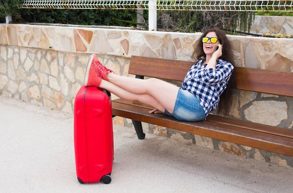 İnsanlar, tatil ve seyahat kavramı - bavul açık havada ayağa ile oturan genç kadın