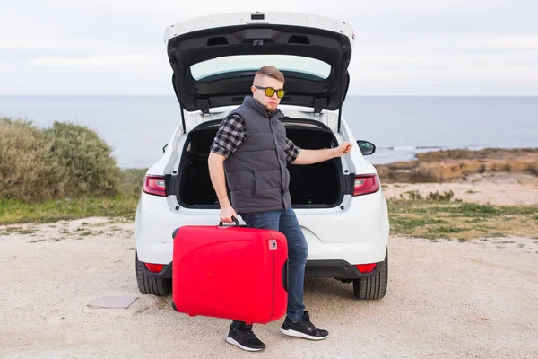 Cestování, cestovní ruch a lidé koncept - šťastný muž v brýlích, stojící nad pozadí přírody poblíž vozu s červenými kufr — Stock fotografie
