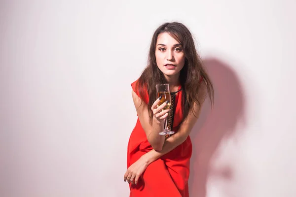 Party, holidays and celebrations concept - Cheerful charming young woman in red dress drinking champagne or wine and dancing over white background