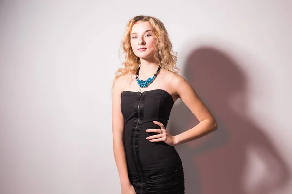 Conceito de moda e modelo - Linda jovem mulher loira sexy em um vestido preto posando contra uma parede branca — Fotografia de Stock