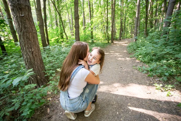 Naturaleza, familia, concepto de personas - Familia y concepto de naturaleza - Hermosa mamá besa a su pequeña hija en la mejilla — Foto de Stock