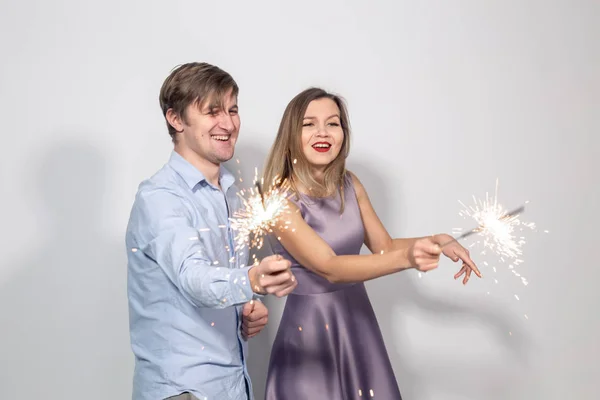 Vacaciones, fiesta y concepto de celebraciones - joven pareja feliz divertida con chispas tonteando sobre fondo blanco — Foto de Stock