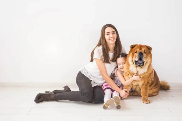 Mascotas, niños y concepto familiar - Niña y su madre abrazando perro chow-chow sobre fondo blanco — Foto de Stock