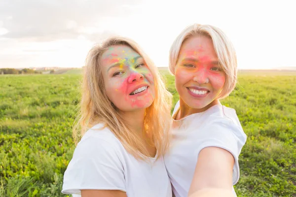 Festival indio de holi, concepto de personas - dos mujeres jóvenes tomando selfie con polvo colorido en las caras —  Fotos de Stock