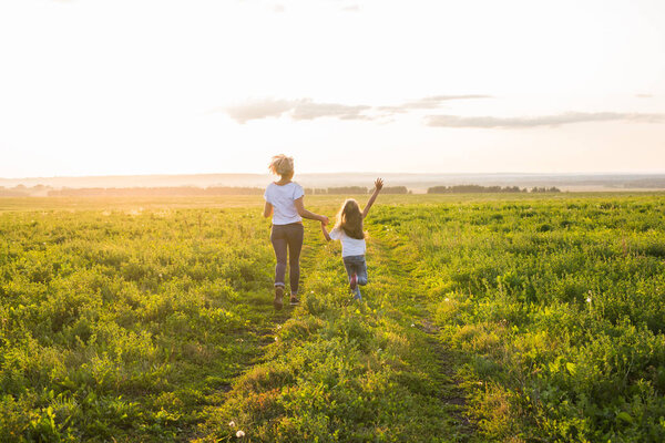 Family, summer and holiday concept - little daughter and mother run in the summer field