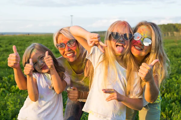 Vacaciones, fiesta holi y concepto familiar - Chicas felices y divertidas cubiertas de pintura en verde gesto de campo pulgares hacia arriba —  Fotos de Stock