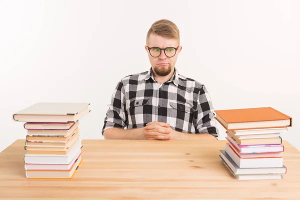 Concepto de personas, conocimiento y educación: estudiante varón cansado sentado a la mesa con montañas de libros y que no quiere estudiar — Foto de Stock