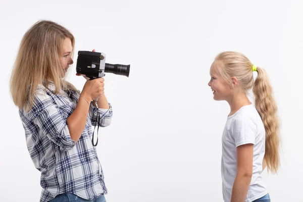 Технологии, фотографирование и концепция людей - блондинка с ретро камерой фотографирует маленькую девочку на белом фоне — стоковое фото