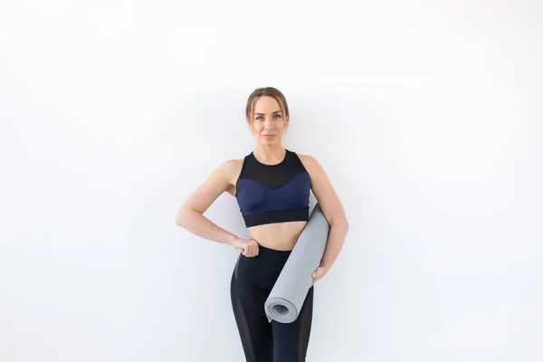 Concepto de personas, fitness y deporte - Mujer atractiva y saludable sosteniendo alfombra gris sobre fondo blanco con espacio para copiar —  Fotos de Stock