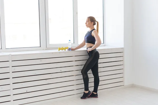 Gente, concepto saludable y deportivo - Retrato de mujer fitness con botella de agua y pesas cerca de la ventana —  Fotos de Stock