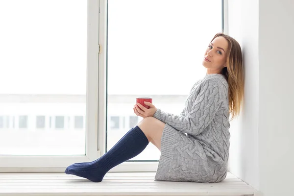 Vár, a magány és a szépség fogalma - fiatal nő csésze forró teát, ablakpárkányon ül — Stock Fotó