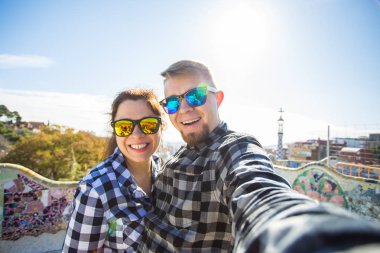 Komik genç çift kamera ile akıllı telefon Park Guell, Barselona, İspanya, gülümseyen fotoğrafı çekmek.