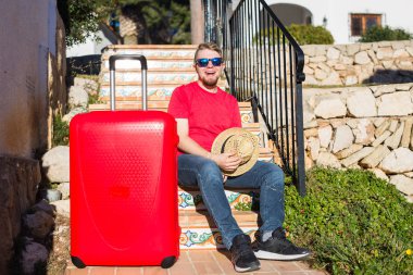 İnsanlar, tatil, seyahat ve dinlenme kavramı - bavulunu yakınındaki merdivenlerde oturan genç adam