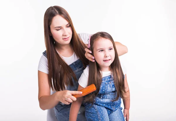 Concepto de familia, maternidad y padres: madre peinando el cabello de sus hijas pequeñas aisladas sobre un fondo blanco — Foto de Stock