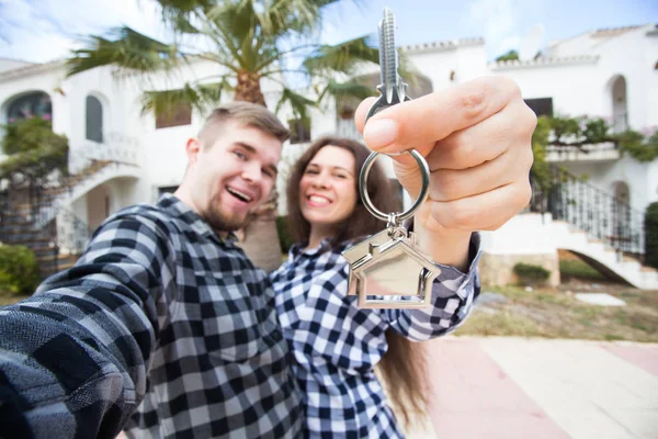 Concepto de bienes raíces y propiedades - Pareja feliz sosteniendo las llaves de un nuevo hogar y casa en miniatura —  Fotos de Stock