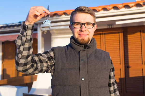 Właściciel domu szczęśliwy. Uśmiechający się młody człowiek gospodarstwa klucze i patrząc na kamery, stojąc na tle nowego domu — Zdjęcie stockowe