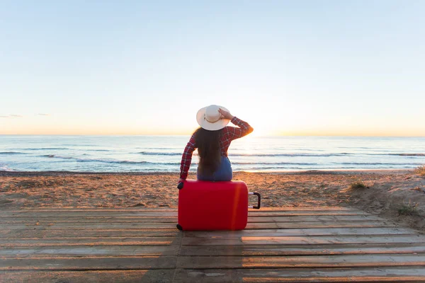 Viaggiare, vacanze e persone concetto - donna felice seduta su una valigia rossa in un cappello di fronte a voi, guardando il mare — Foto Stock