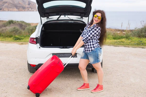 Dovolená, cestování a turistiku koncept - mladá žena s červeným kufr na cestě autem — Stock fotografie