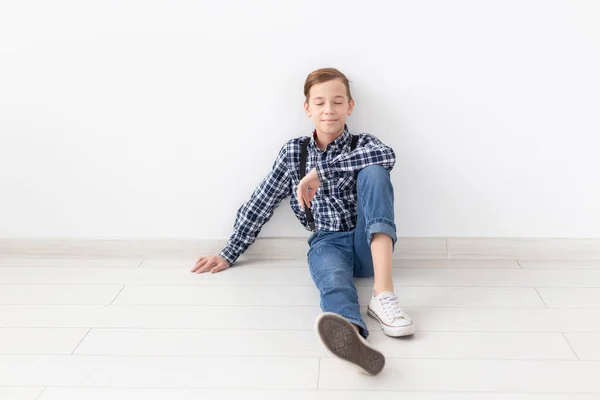 Tinédzser, a gyermekek és a divat fogalma - divatos fiú ül emeleti felett fehér háttér — Stock Fotó
