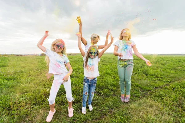 Vacaciones, fiesta holi y concepto de amistad - Saltar mujeres felices y niños cubiertos de pintura —  Fotos de Stock