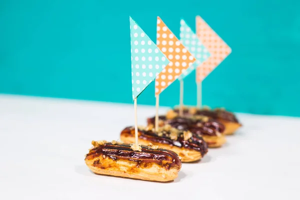 Продукты питания, десерт и вкусная концепция - Шоколадные эклеры украшены как маленький корабль на синем фоне — стоковое фото