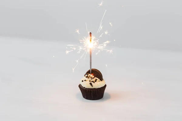 Essen, Bäckerei, Urlaub, Happy Birthday und Dessertkonzept - leckere Cupcake mit Wunderkerze und Plätzchen auf weißem Tisch — Stockfoto