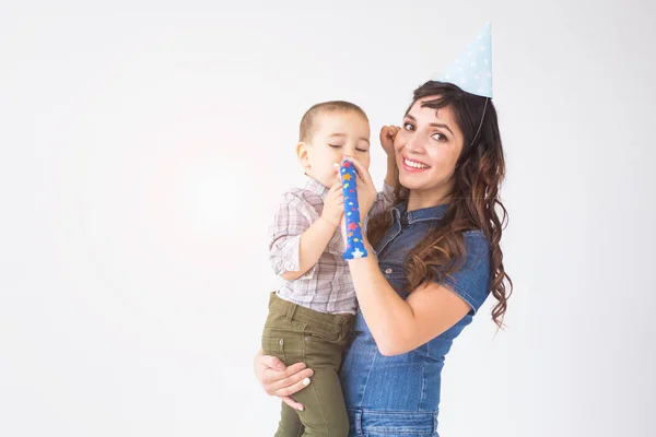 Concepto de niños, familia y vacaciones - madre joven en sombrero de cumpleaños sosteniendo al pequeño hijo sobre un fondo blanco — Foto de Stock