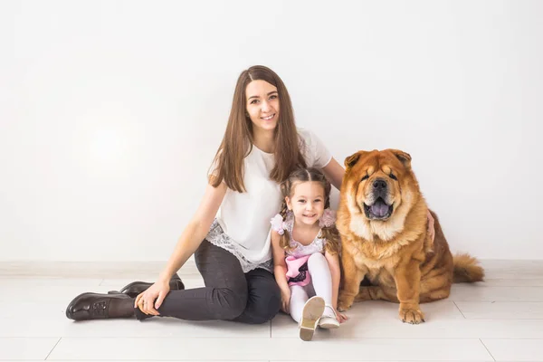 Mascotas, niños y concepto familiar - Niña y su madre abrazando perro chow-chow sobre fondo blanco —  Fotos de Stock