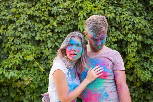 Concepto de vacaciones, vacaciones y personas - Pareja feliz divirtiéndose con polvo multicolor en sus caras — Foto de Stock