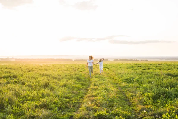 Koncepcja rodziny, lato i wakacje - matka trzyma rękę córki, uruchomiona w zielone pola — Zdjęcie stockowe