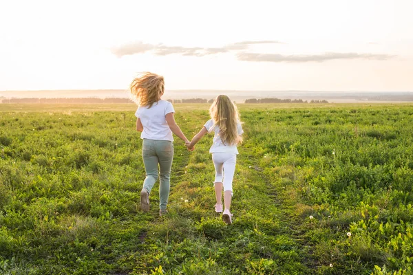 Familj, sommar och semester koncept - Back syn på modern som håller hennes döttrar hand kör mot ljus — Stockfoto