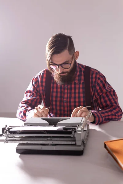 Gente y concepto de tecnología - Día Mundial del escritor, hombre guapo con barba trabajando en la máquina de escribir sobre fondo negro — Foto de Stock