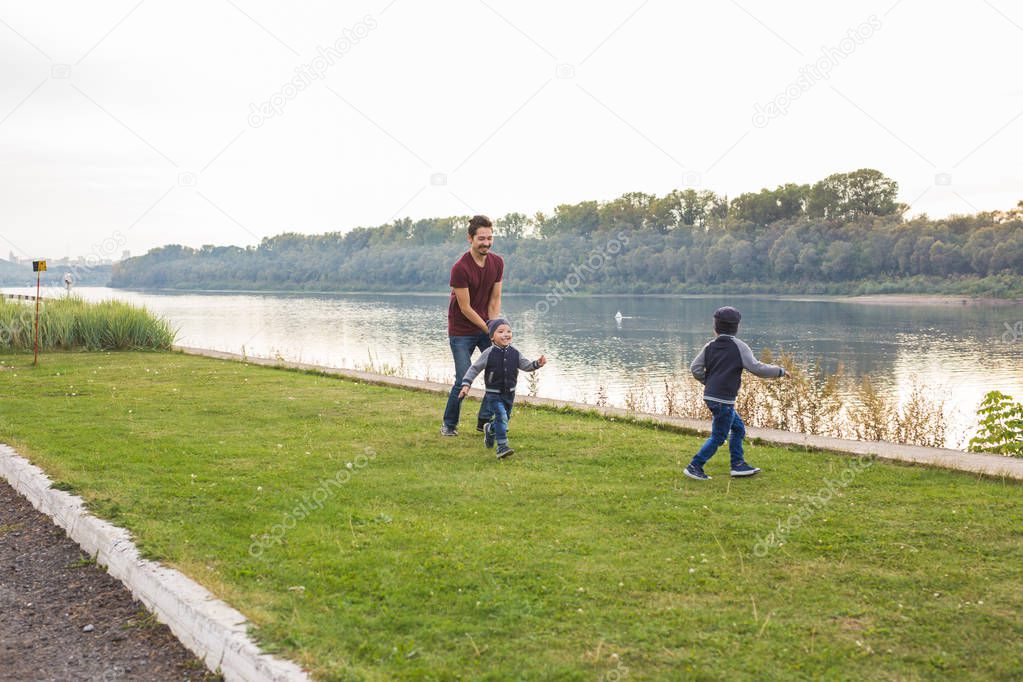 Childhood, family concept - father playing with two sons near the lake