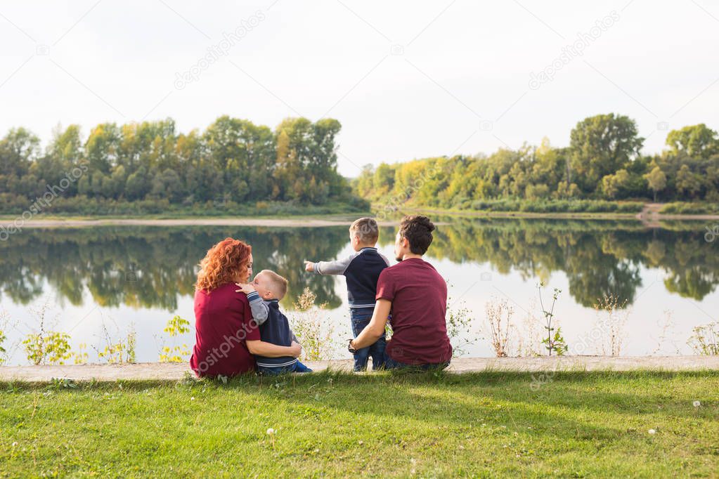 Parenthood, nature, people concept - family with two sons sitting near the lake