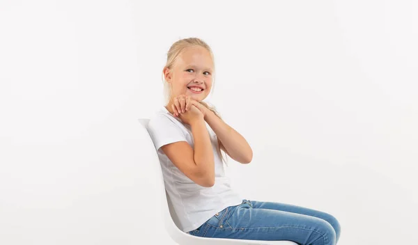 Adorable niña pequeña con el pelo largo y rubio sentado en la silla sobre fondo blanco — Foto de Stock