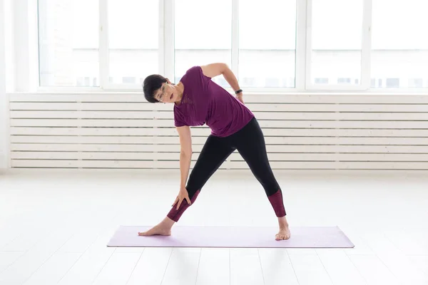 Deporte, yoga, concepto de personas - Mujer deportiva de mediana edad practicando yoga en interiores —  Fotos de Stock