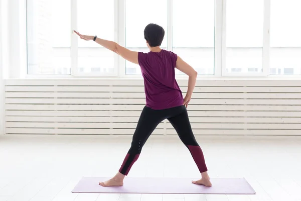 Deporte, yoga, concepto de personas - Mujer deportiva de mediana edad practicando yoga en interiores — Foto de Stock